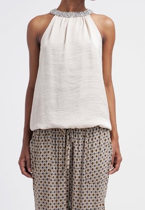 Ærmeløs hvid haltertop med perlebesat hals, kombineret med beige mønstrede løse bukser med snøre og forlommer.