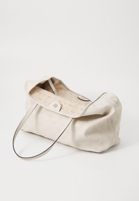 Sac à main beige texturé avec un motif en relief subtil, deux poignées et un intérieur doublé avec un design imprimé. Fermeture à bouton sur le dessus.