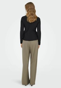 Mustapukuinen pitkähihainen toppi, jossa on vartalonmyötäinen vyötärö, yhdistettynä väljiin khakinvärisiin housuihin, joissa on suora leikkaus ja hienovarainen tekstuuri.