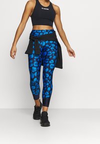 Blå leopardmönstrade leggings gjorda av stretchigt tyg, ihop med en svart kort topp och en knuten svart jacka, avslutat med svarta träning-skor.