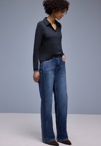 Chemise noire boutonnée et jean large bleu avec coutures latérales blanches, offrant une coupe décontractée et une texture lisse.