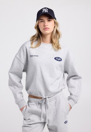 Sweat-shirt gris en coton avec le texte "RESET MODE" ; présente des épaules tombantes et des poignets côtelés. Associé à un jogging gris et une casquette de baseball bleu marine.