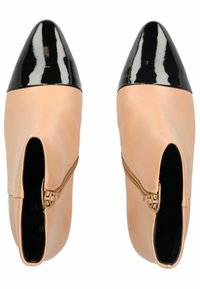 Botines de cuero nude con punta en charol negro brillante, que cuentan con una cremallera lateral y un diseño elegante y aerodinámico.