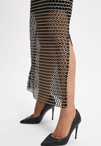 Schwarz-beige gemustertes Mesh-Kleid mit hexagonalem Muster und seitlichem Schlitz, kombiniert mit eleganten schwarzen Stiletto-Absätzen.