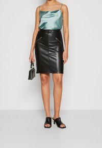 Svart faux läder pencilkjol med framfickor med dragkedja, ihopparad med en teal satin camisole och svarta öppna tå klackskor.