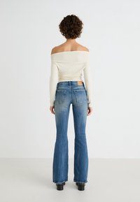 Top blanco sin hombros de manga larga combinado con jeans de campana de tiro medio en azul, que presentan un degradado de claro a oscuro y dos bolsillos traseros.