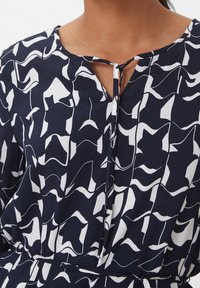 Vestido de fondo marino con patrones que presentan formas abstractas en blanco, escote con muesca y detalle de lazo en el cuello. Textura de tela suave.