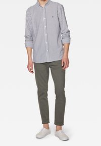 Camisa de botones a rayas en azul marino y blanco, combinada con jeans ajustados verde olivo y zapatillas blancas, que presenta un cuello clásico y mangas enrolladas.
