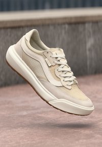 Beige idrettssko med mesh og semsket skinn detaljer, rund tå, hvit såle, og kontrasterende grå detaljer. Lett og pustende design.