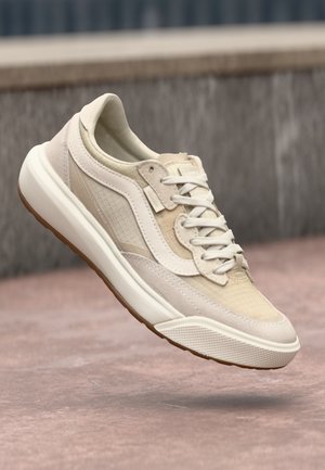 Beige idrettssko med mesh og semsket skinn detaljer, rund tå, hvit såle, og kontrasterende grå detaljer. Lett og pustende design.