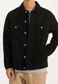 Svart denimjacka med silverfärgade tryckknappar, två bröstfickor och sidfickor. Har en ren design och texturerad tyg.