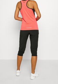 Top deportivo sin mangas en color rosa con detalles en negro, combinado con pantalones cortos negros con puños elásticos; incluye una franja reflectante en la parte trasera.