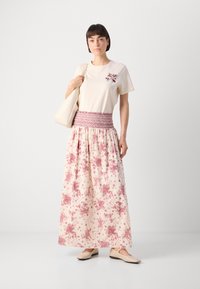 Cream t-shirt with maroon floral embroidery, paired with a long, flowing skirt featuring pink floral patterns and smocked waistband. Plain beige flats.