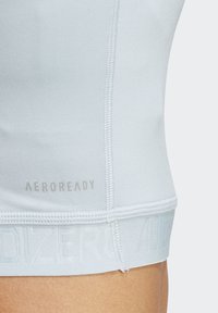 Lyseblå sportstanktop lavet af glat, strækbart materiale. Har "AEROREADY"-logo, flade sømme og en tætsiddende pasform.
