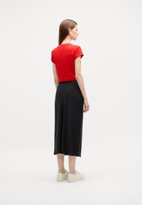 Červený krátký rukáv cropped top v kombinaci s dlouhou černou sukní. Sukně má hladkou texturu a outfit je doplněn světle barevnými teniskami.