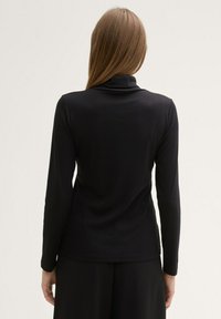 Schwarzes langärmliges Oberteil aus einem weichen, dehnbarem Material; verfügt über einen hohen Kragen und eine figurbetonte Silhouette.