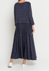 Marinblå tvådelad outfit bestående av en strukturerad kort tröja och en lång, plisserad kjol med en åtsittande midja, i kombination med vita sneakers.