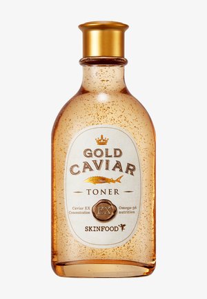 Flacon ambre transparent avec bouchon doré contenant un toner aux flocons d’or étiqueté Gold Caviar Toner par Skinfood.