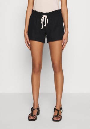 Shorts noirs avec une taille froncée et un cordon de serrage, en tissu léger. Associés à des sandales noires à lanières.
