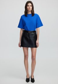 Blauwe korte mouwen t-shirt met ronde hals, gecombineerd met een zwarte leren minirok met een gesp riem en voornaad detail.