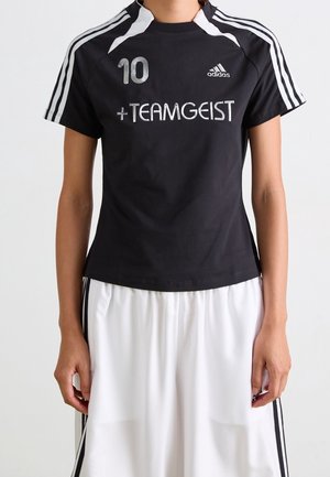 Person trägt schwarzes Adidas Sportshirt mit der Nummer 10 und dem Text "TEAMGEIST", kombiniert mit weißen Shorts mit schwarzen Streifen.