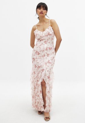 Lys pinket blomster maxi kjole med spaghetti stropper, flæser, høj slidser og en tætsiddende overdel. Materialet virker gennemskinneligt og delikat.