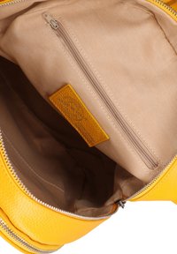 Sac en cuir jaune avec intérieur en tissu beige, comprenant une poche zippée et une étiquette de marque en cuir jaune cousue à l'intérieur.