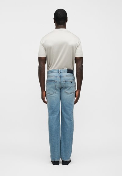 Τζιν σε ίσια γραμμή ανοιχτό μπλε με υφή, πέντε τσέπες και μαύρο δερμάτινο ταμπελάκι στην πλάτη, φορεμένα με ανοιχτό γκρι μπλουζάκι.