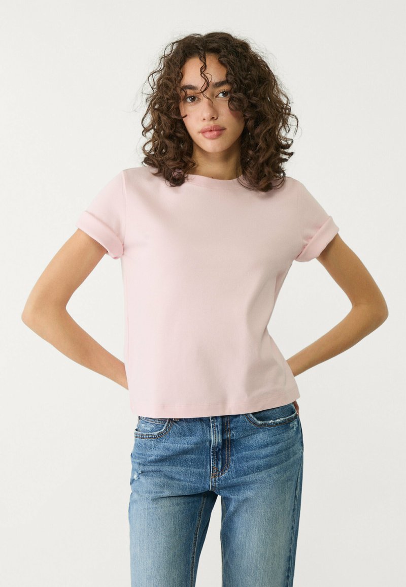 Lys pink kortærmet t-shirt med rund hals og rullede ærmer, lavet af glat stof, kombineret med blå denim jeans.