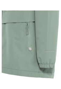Manche et côté de veste vert clair avec une poche zippée verticale et un poignet élastique, affichant un texte subtil de la marque sur la manche.
