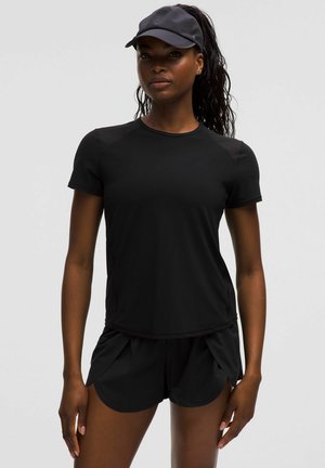 Athletic woman wearing black short-sleeve shirt, black running shorts, and black visor, standing against a plain light background.