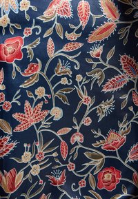 Blomstret stof med røde og beige blomster og blade på en marineblå baggrund, med indviklede konturer og detaljer, glat tekstur.