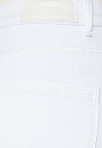 Bijela denimska tkanina sa suptilnom teksturom, s detaljima šivanja na šavu i pravokutnom off-white etiketom s ugraviranim natpisom "VERO MODA".