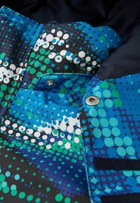 Bunt gemustertes Textil mit einem Muster aus blauen, grünen und weißen Punkten auf schwarzem Hintergrund, mit silbernen Druckknöpfen und Klettverschluss.