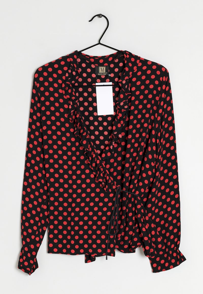 Black blouse with red polka dots, featuring a ruffled neckline, long sleeves, and a tie closure at the waist. Smooth fabric, casual design.