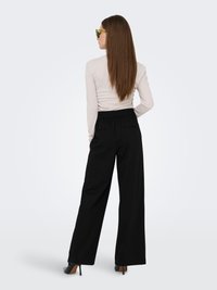 Top crema ajustado de manga larga combinado con pantalones negros sueltos de cintura alta y tacones de aguja negros. La modelo lleva gafas de sol de color verde claro.