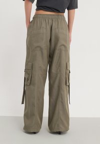 Weite Cargo-Hosen aus olivgrünem Material. Mit elastischem Bund, großen Gesäßtaschen und seitlichen Cargo-Taschen. Glatte Textur.