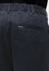 Gros plan d'un pantalon foncé avec une taille élastique et une poche arrière étiquetée Barbour.