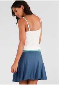 Camisola bianca a spalline sottili sovrapposta a una maglietta azzurro chiaro, abbinata a una gonna blu svasata al ginocchio. Tessuto morbido e fitting casual.