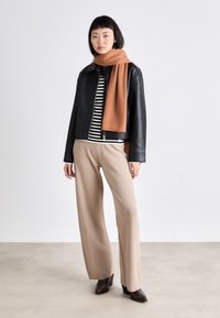 Veste en cuir noir portée sur un haut à manches longues rayé, pantalon beige à jambes larges, et une écharpe marron. Des chaussures à talons marron complètent le look.