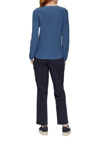 Blauer, gerippter Langarmpullover mit einem runden Ausschnitt, kombiniert mit dunklen Cargo-Hosen und schwarzen Schuhen mit hellen Sohlen.