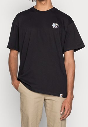 T-shirt en coton noir à coupe relaxed, manches courtes, un motif géométrique en forme de cube sur le côté gauche de la poitrine, et une étiquette à l'ourlet.