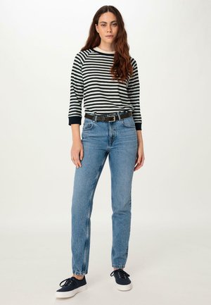Maglietta a maniche lunghe a righe bianche e nere, jeans a vita alta blu, cintura nera e sneakers blu navy con suola bianca. Design semplice e vestibilità casual.