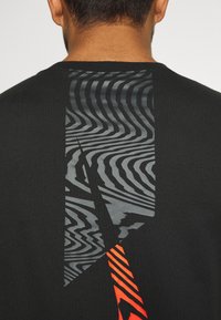 Černé tričko s geometrickým designem v šedé a jasně oranžové barvě na zadní straně, s vlnitými vzory a ostrými liniemi. Hladká textura.