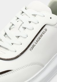 Λευκό δερμάτινο αθλητικό παπούτσι με ανοιχτό μπλε κορδόνια, καφέ ραφές σε αντίθεση και το λογότυπο "KARL LAGERFELD" στο πλάι. Λείο, μινιμαλιστικό σχέδιο.
