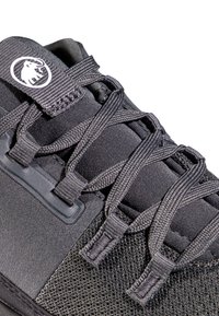 Svart träningssko med texturerad ovandel, utrustad med integrerade snörningar, en vadderad krage och en logotyp-accent på tungan.