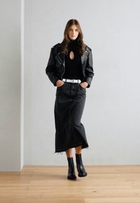 Veste de moto en cuir noir sur un col roulé noir, associée à une jupe en denim noir et des bottines, avec une ceinture blanche en accent.