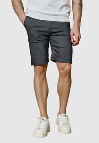Shorts gris avec un design à l'avant plat, coupés au niveau des genoux, et poches latérales, fabriqués à partir d'un tissu lisse. Portés avec des baskets blanches.