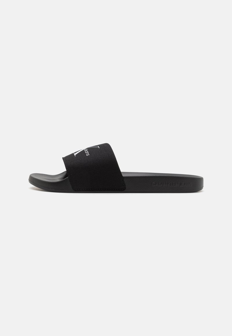 Sorte slidesandaler i svart med en myk stoffrem med hvit logo, flate gummisåler og et minimalistisk design.