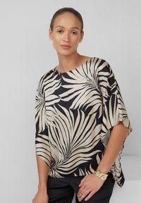 Vloeiende blouse in zwart en crème, met een palmbladpatroon. De stof heeft een gladde textuur en brede mouwen die losjes vallen.